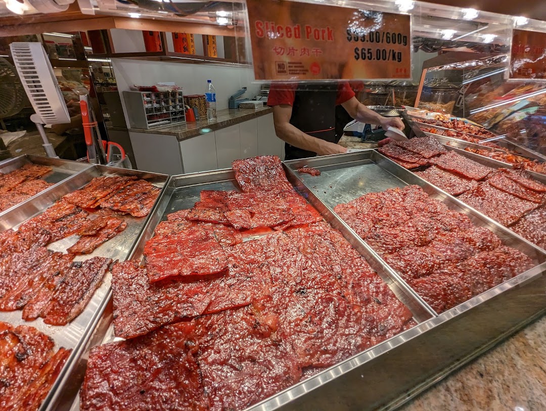A vibrant display of freshly prepared bak kwa (sliced pork jerky) at Bee Cheng Hiang, with a staff member serving.