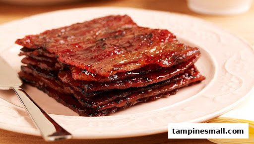 A stack of glossy, caramelized bak kwa (BBQ meat slices) on a light pink plate.