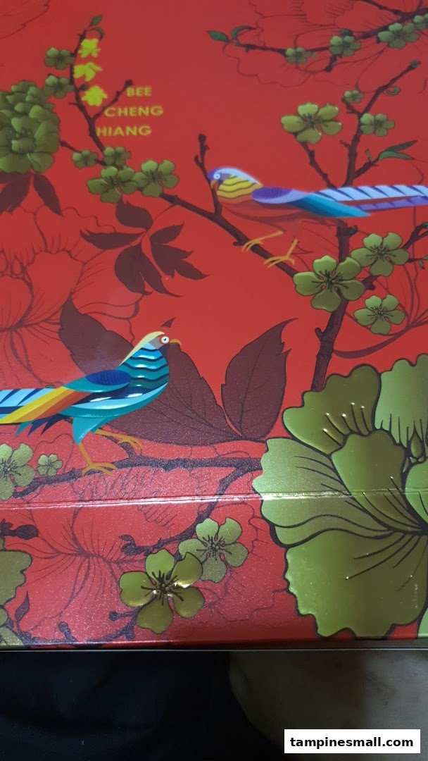 A vibrant red box featuring intricate bird and floral designs, showcasing the Bee Cheng Hiang brand.