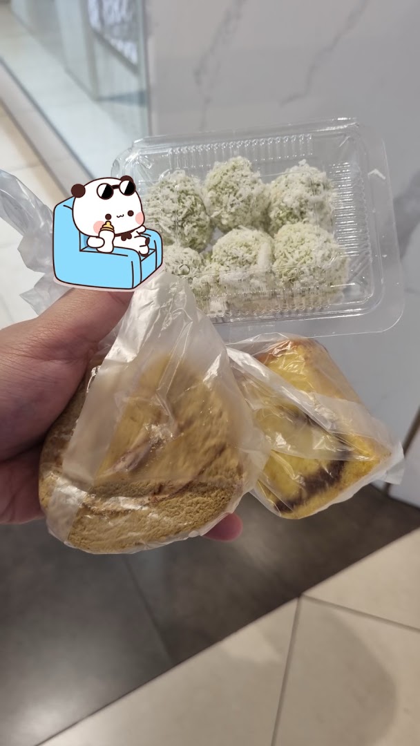 A hand holds a clear container of green coconut-covered sweets and two individually wrapped cakes.