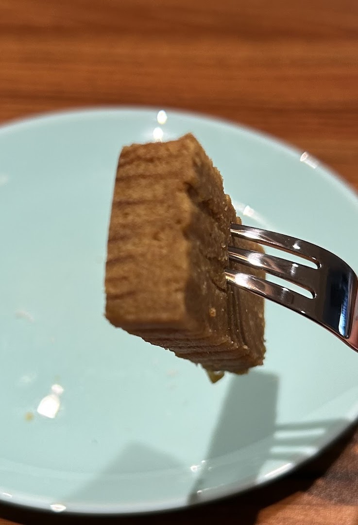 A delicious piece of layered cake, likely Lapis Legit, on a fork over a light blue plate.