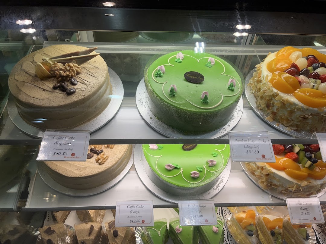 A vibrant display case showcasing various delicious cakes, including Coffee Cake, Pandan Kaya Cake, and Fruit Gateau, with prices.