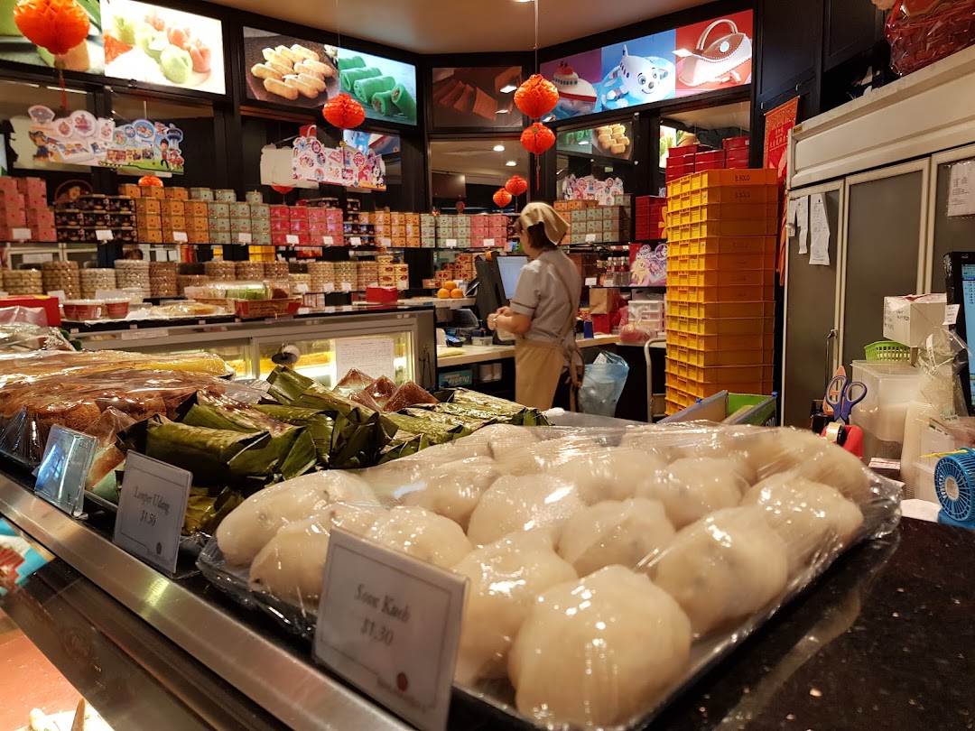 Interior view of Bengawan Solo showcasing a wide array of traditional Indonesian snacks and pastries, with a staff member at the counter.