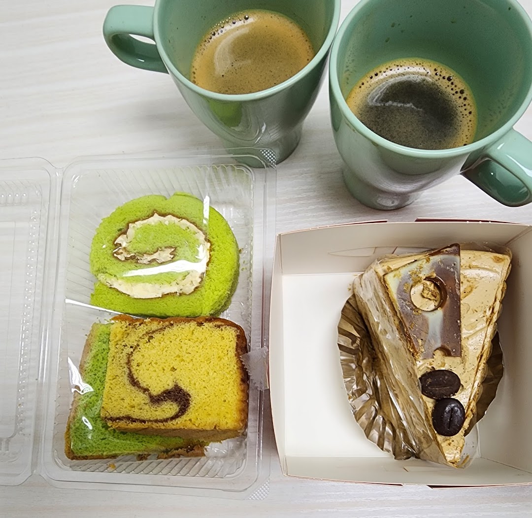 Two cups of coffee accompany a selection of cakes, including a green roll cake and a coffee-flavored slice.