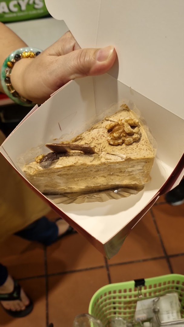 A hand holds a slice of cake in a white takeaway box, featuring walnuts and chocolate.