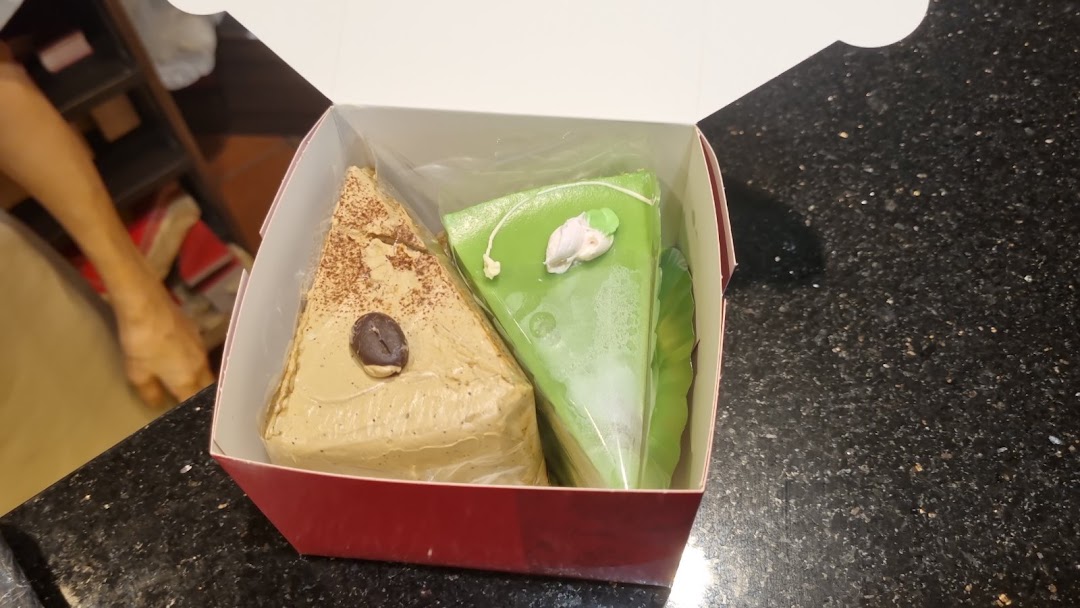 Two slices of cake, one coffee-flavored and one green, in a takeaway box.