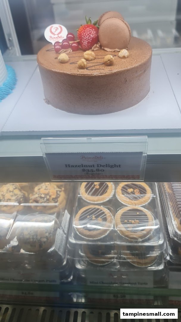 A delicious chocolate cake with berries and nuts, alongside mini tarts, displayed in a bakery case.