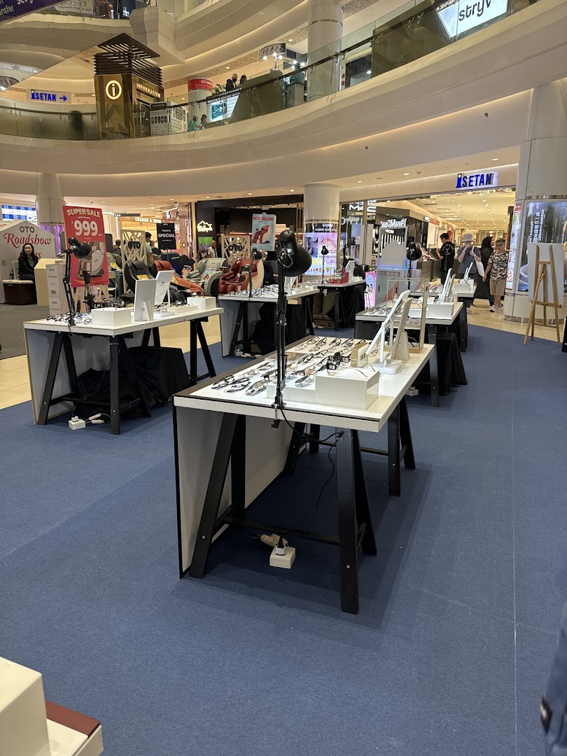 Eyeglass displays showcasing various frames in a mall's common area, with other retail stores in the background.