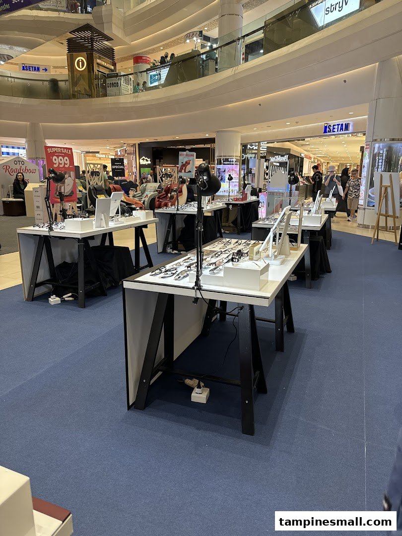 Eyeglass displays showcasing various frames in a mall's common area, with other retail stores in the background.