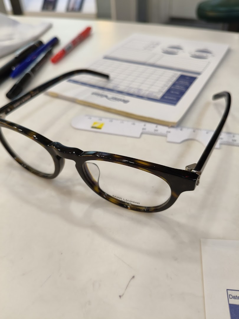 A pair of stylish Saint Laurent eyeglasses on a table, with office supplies in the background.