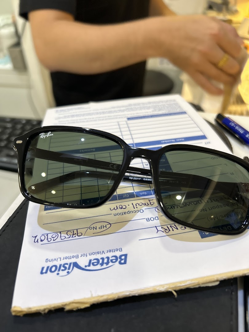 A pair of Ray-Ban sunglasses rests on a Better Vision customer form, with a staff member in the background.