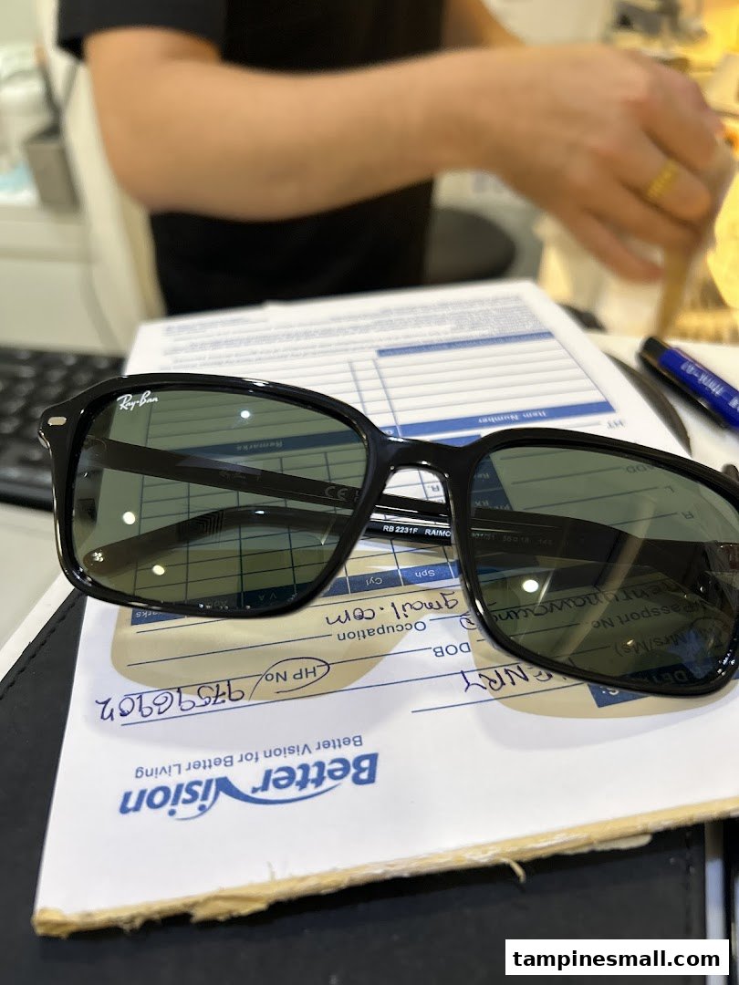 A pair of Ray-Ban sunglasses rests on a Better Vision customer form, with a staff member in the background.