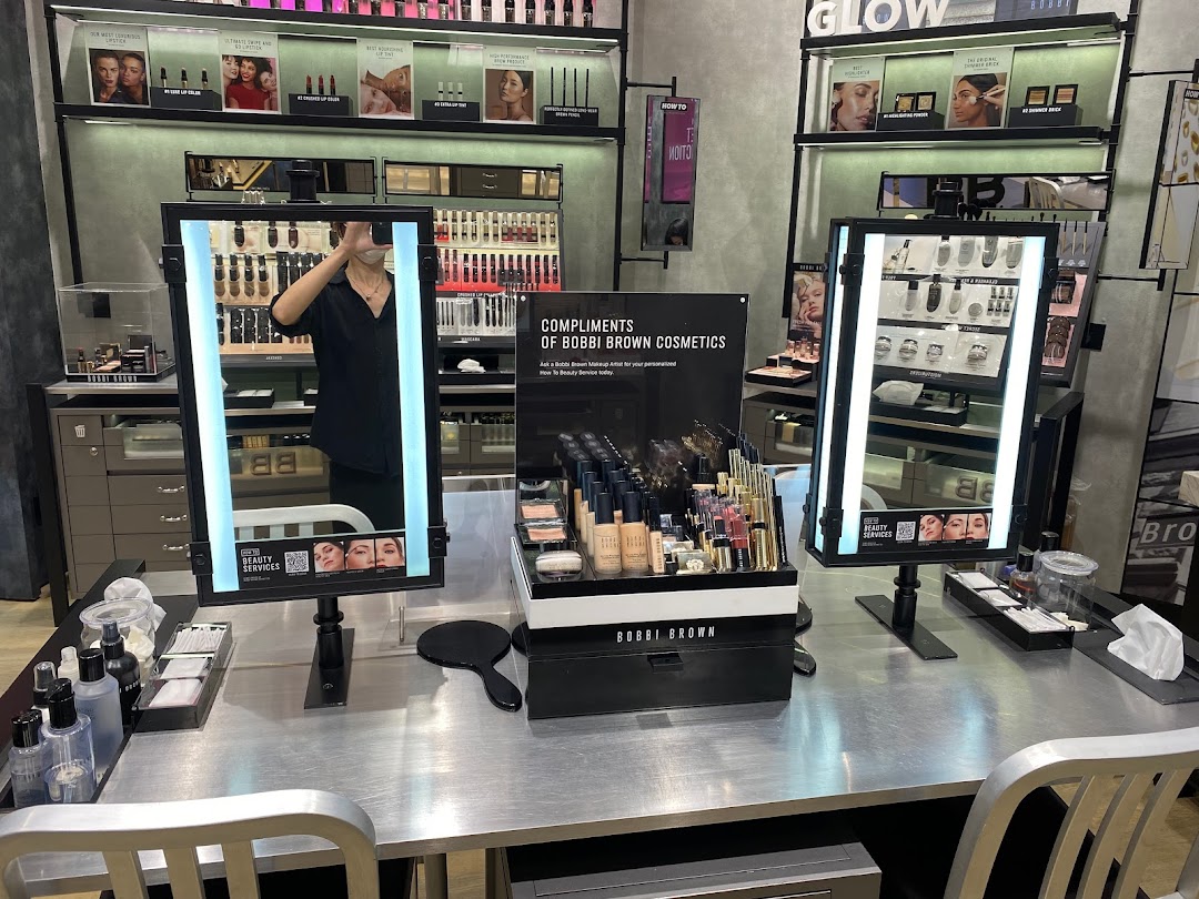 A well-lit Bobbi Brown makeup counter featuring a wide array of cosmetics, mirrors, and beauty services setup.