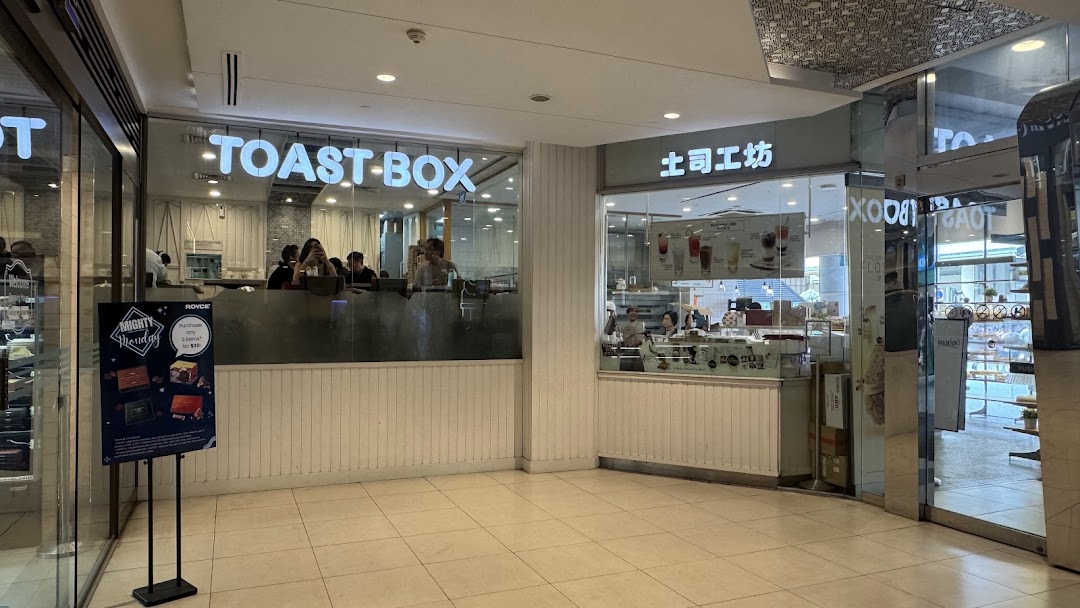 The exterior of Toast Box, a cafe, with its illuminated sign and visible interior seating.