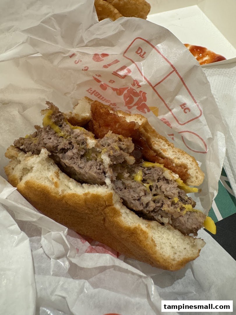 A close-up of a half-eaten Burger King burger with hash browns in a wrapper.