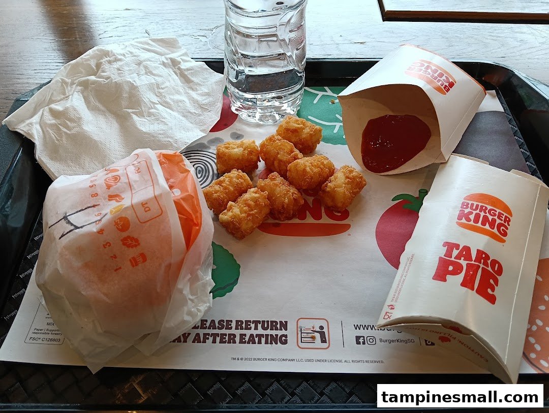 A Burger King meal on a tray, featuring a burger, tater tots, a Taro Pie, and a drink.