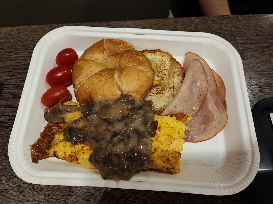 A breakfast platter featuring scrambled eggs with mushrooms, ham, croissant, and cherry tomatoes.