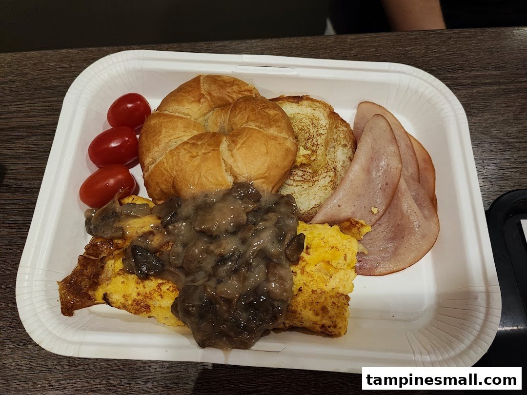 A breakfast platter featuring scrambled eggs with mushrooms, ham, croissant, and cherry tomatoes.