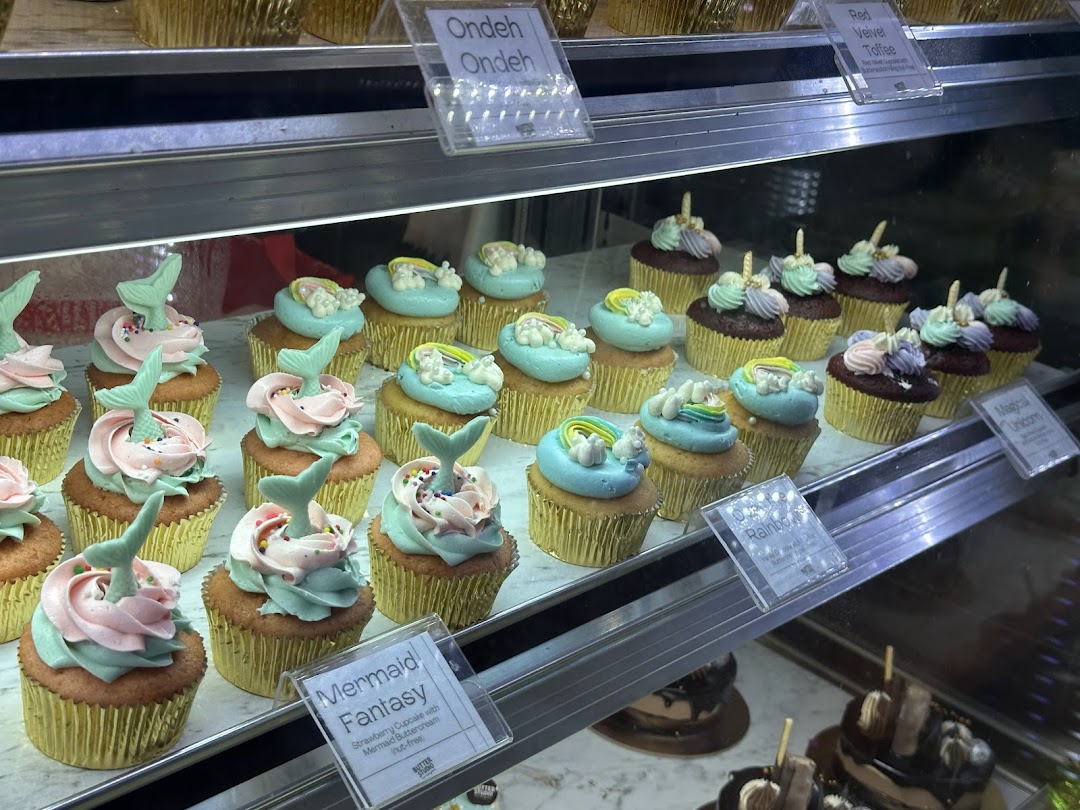 A vibrant display of beautifully decorated cupcakes, including Mermaid Fantasy and Unicorn designs, in a bakery showcase.