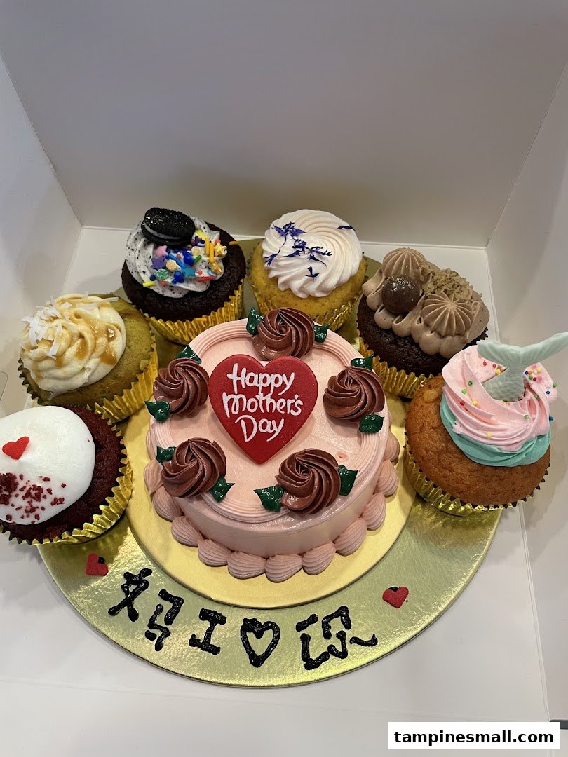 A delightful assortment of cupcakes surrounding a 'Happy Mother's Day' cake in a box.