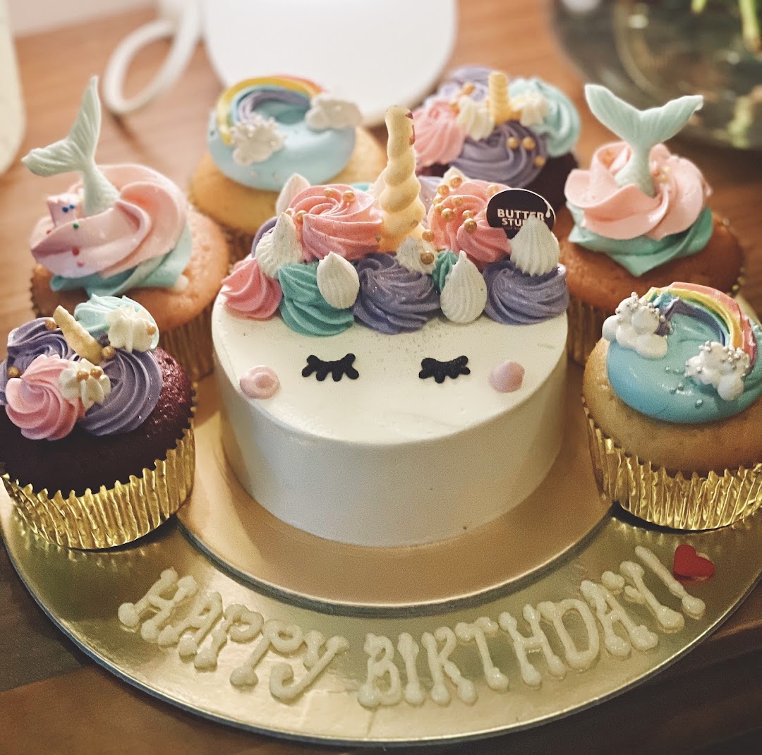 A delightful unicorn cake surrounded by colorful, whimsical cupcakes on a 'Happy Birthday' platter.