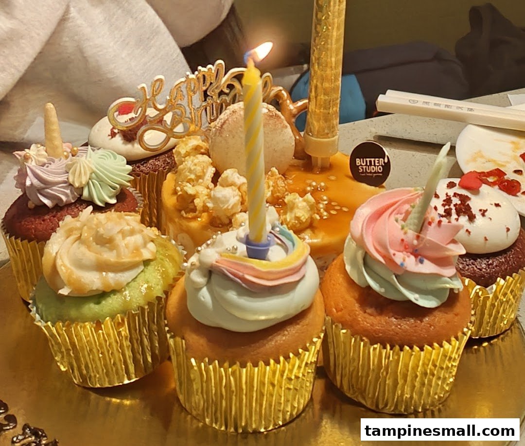 A vibrant assortment of decorated cupcakes with birthday candles and a 'Happy Birthday' topper.