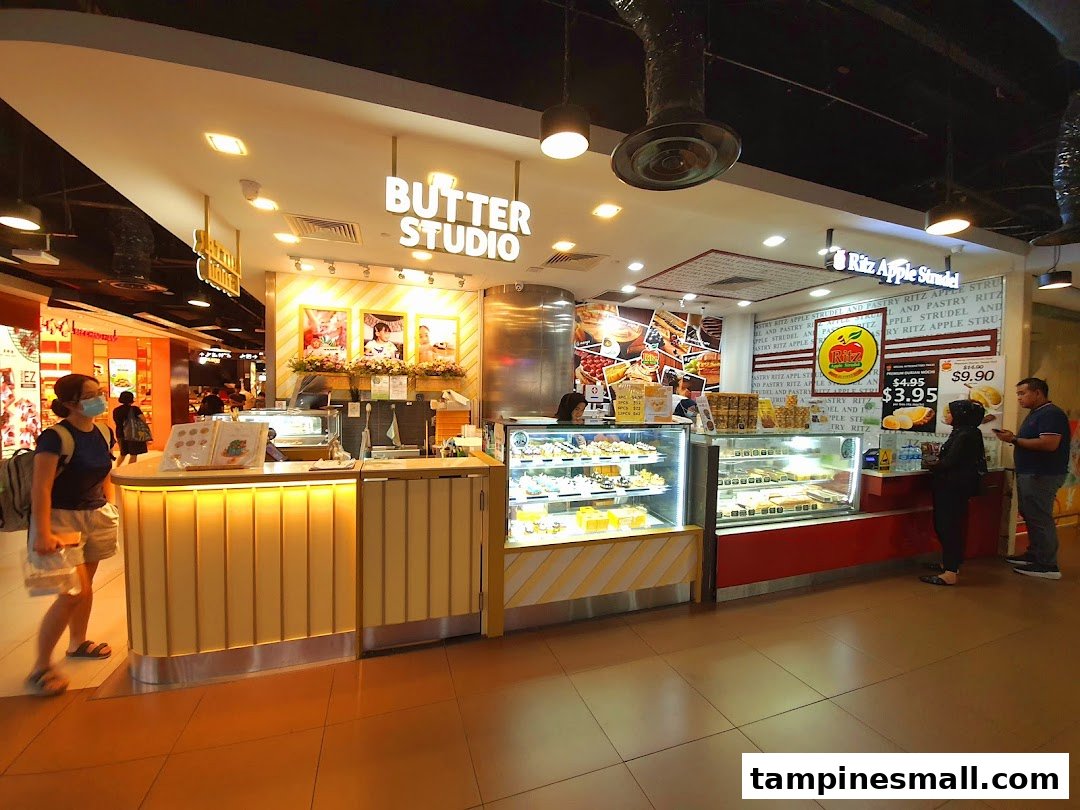 A vibrant Butter Studio shop front showcasing delicious cakes, pastries, and Ritz Apple Strudel.