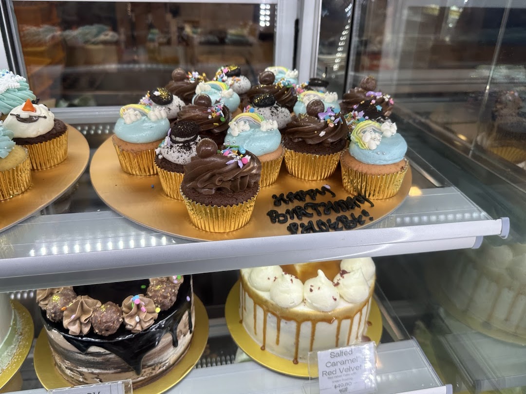 A vibrant display of beautifully decorated cupcakes and cakes in a glass showcase at Butter Studio.
