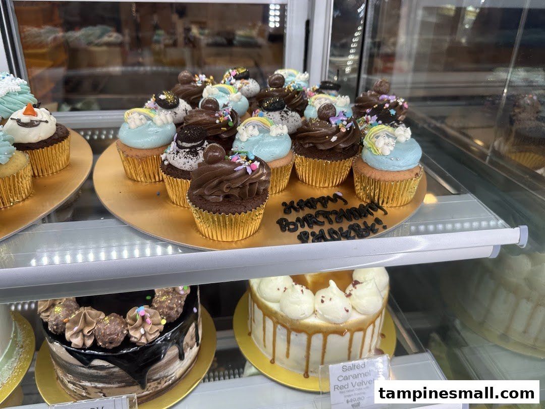 A vibrant display of beautifully decorated cupcakes and cakes in a glass showcase at Butter Studio.