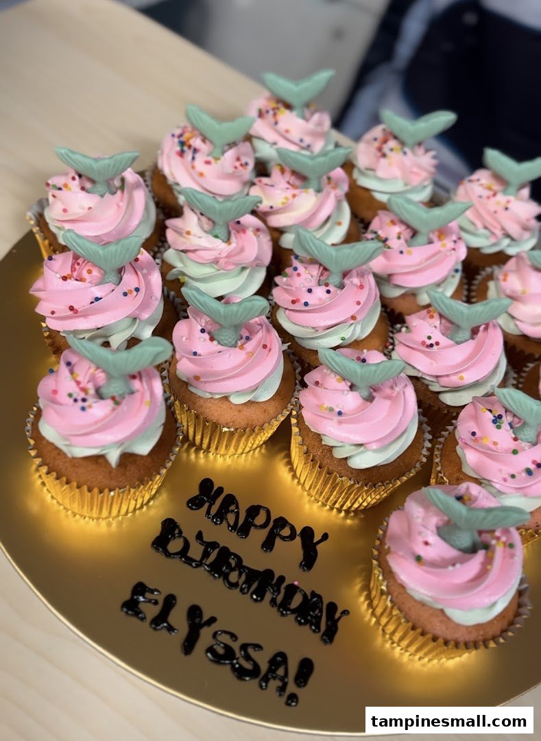 A golden platter filled with pink and mint green mermaid-themed cupcakes with sprinkles and a 'Happy Birthday Elyssa!' message.