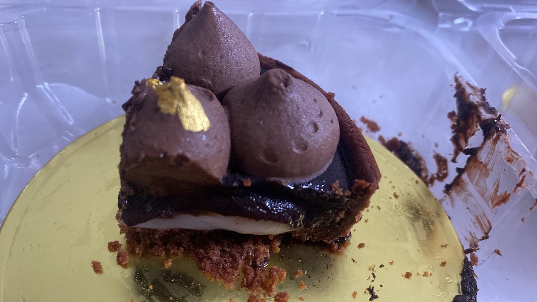 A decadent chocolate tart with chocolate cream and gold leaf, presented in a clear container.