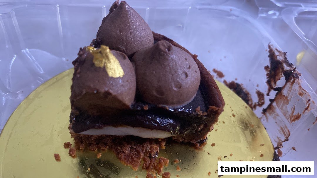 A decadent chocolate tart with chocolate cream and gold leaf, presented in a clear container.