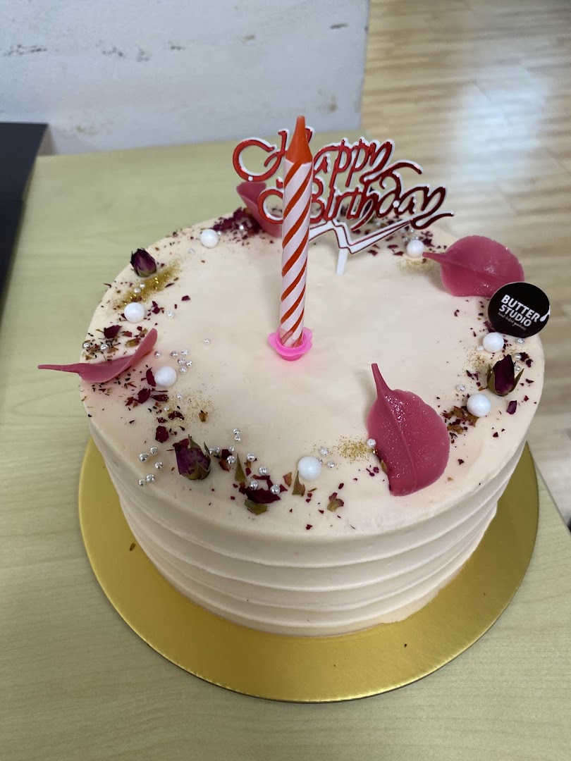 A beautifully decorated birthday cake from Butter Studio with a candle and 'Happy Birthday' topper.