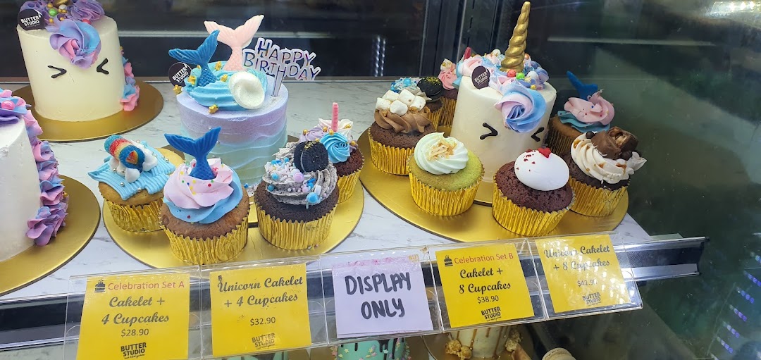 A vibrant display of custom cakes and cupcakes, including unicorn and mermaid themes, with pricing for celebration sets.