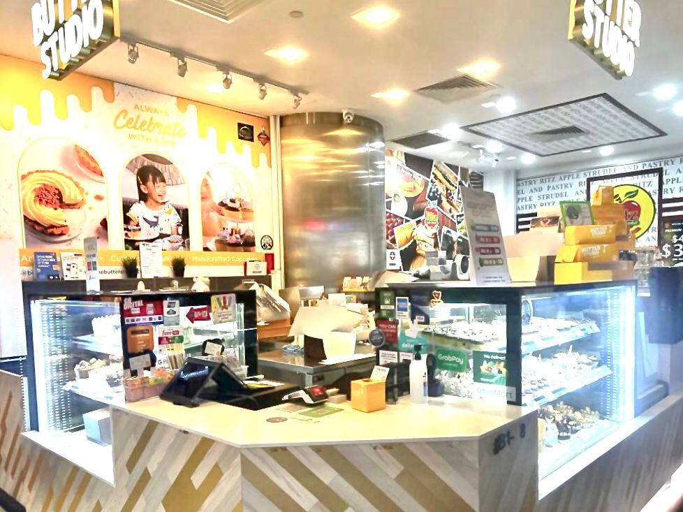 An inviting interior view of Butter Studio, showcasing dessert display cases, a service counter, and vibrant wall decor.