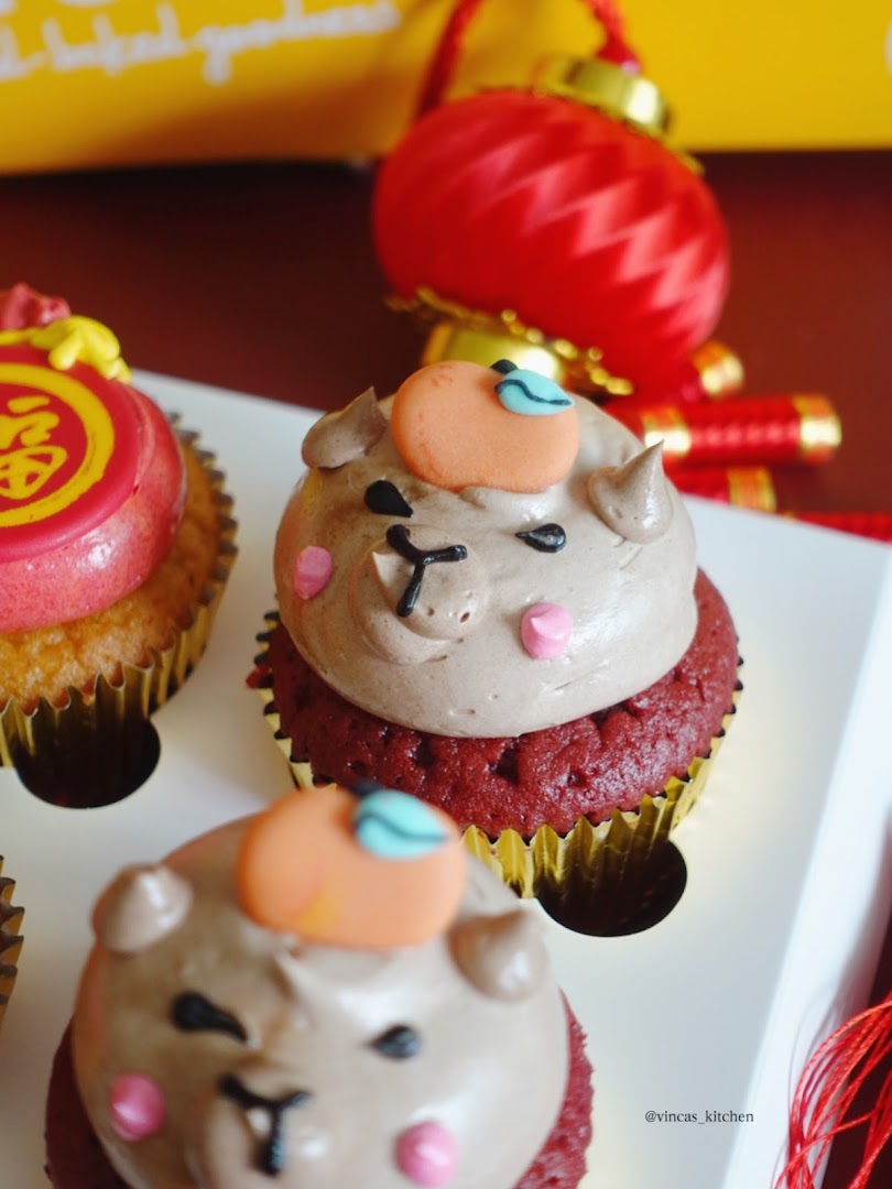Close-up of festive red velvet cupcakes with cute animal frosting and a mandarin orange decoration.