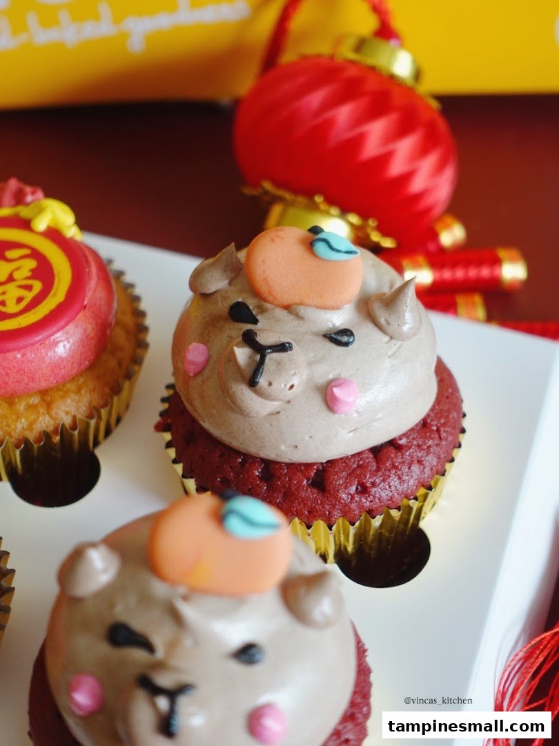 Close-up of festive red velvet cupcakes with cute animal frosting and a mandarin orange decoration.