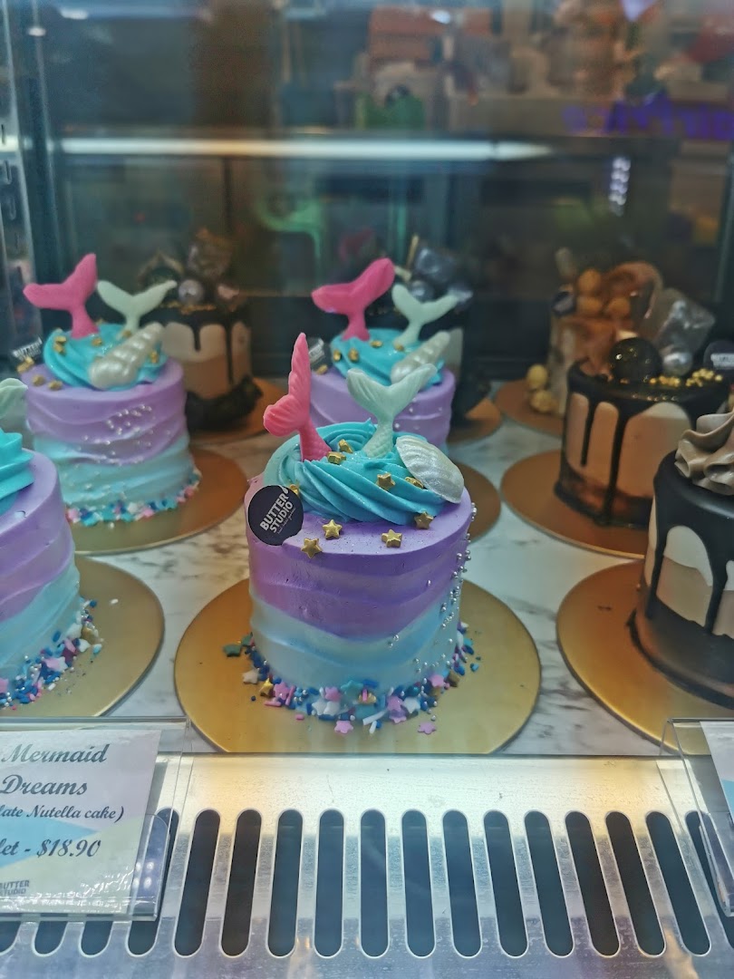 A display of beautifully decorated mini cakes, including 'Mermaid Dreams', in a glass showcase.
