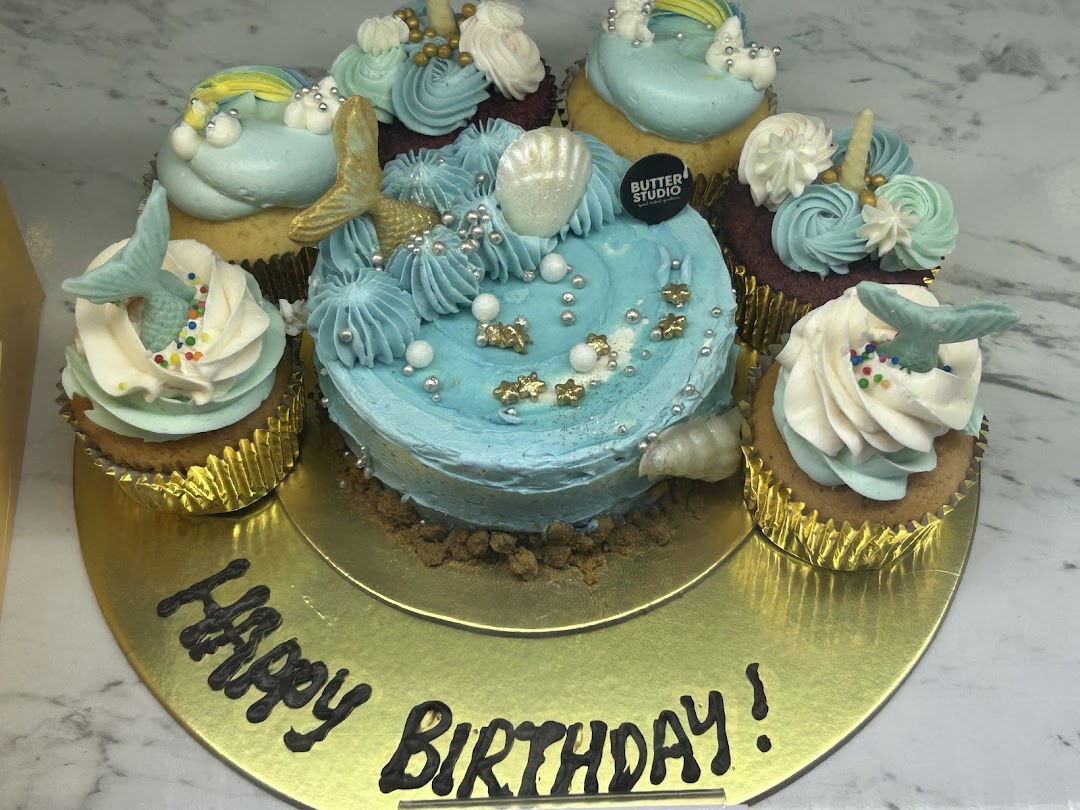 A mermaid-themed birthday cake surrounded by matching cupcakes on a gold platter.