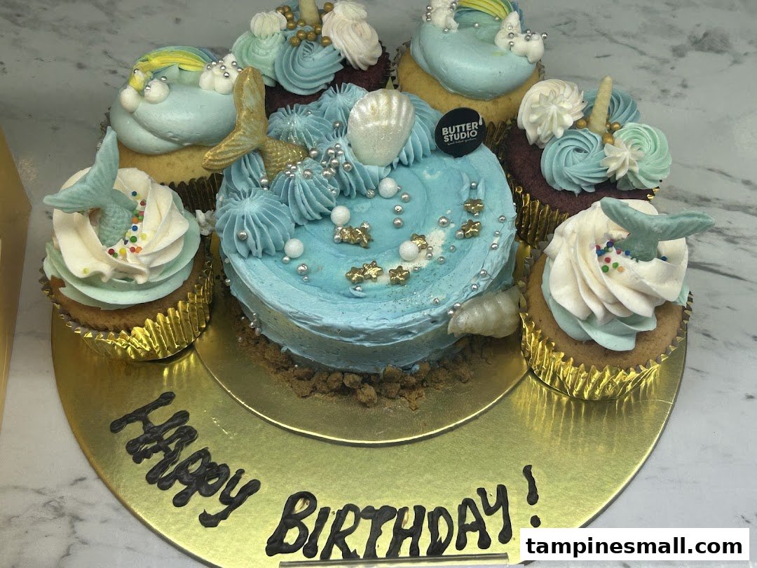 A mermaid-themed birthday cake surrounded by matching cupcakes on a gold platter.