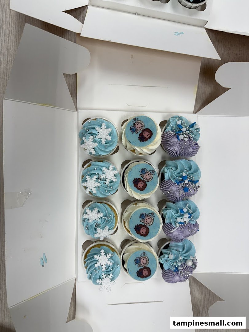A dozen themed cupcakes in a white box, featuring blue, purple, and character designs.