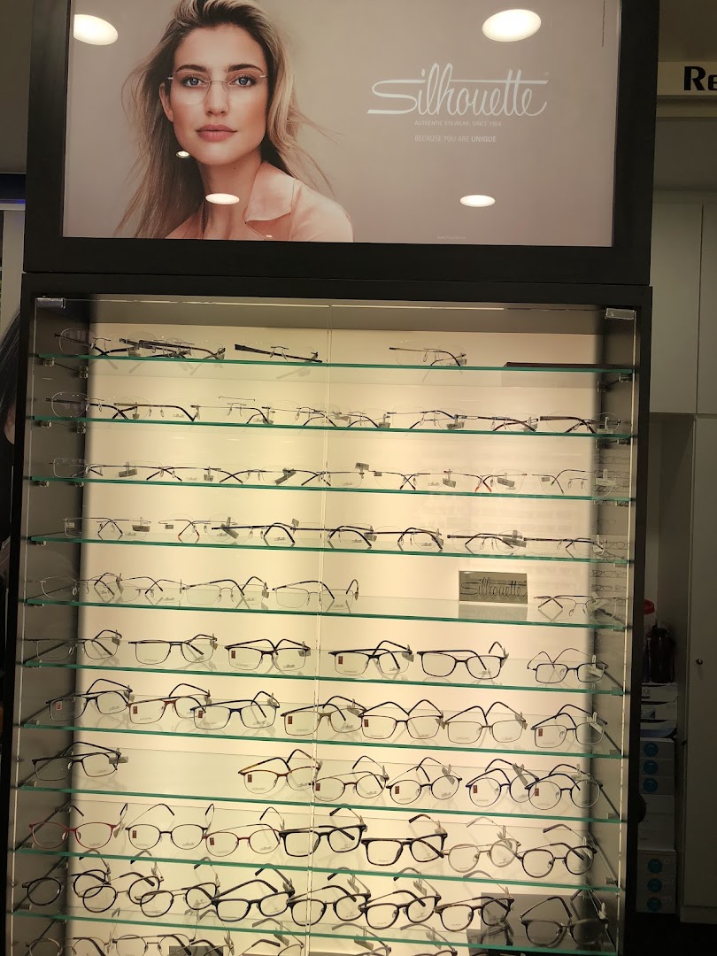 A brightly lit display case showcasing numerous pairs of eyeglasses, with a 'Silhouette' brand advertisement above.