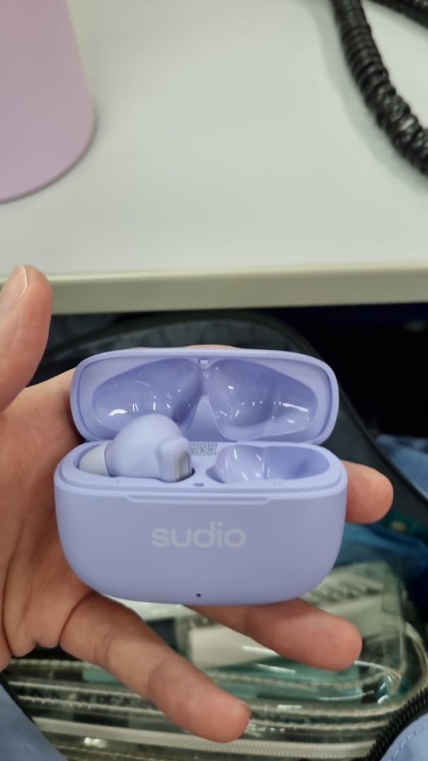 A hand holds a pair of lavender Sudio wireless earbuds in their open charging case.
