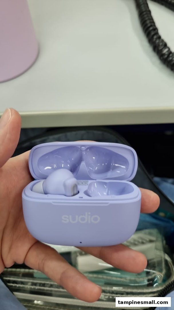 A hand holds a pair of lavender Sudio wireless earbuds in their open charging case.