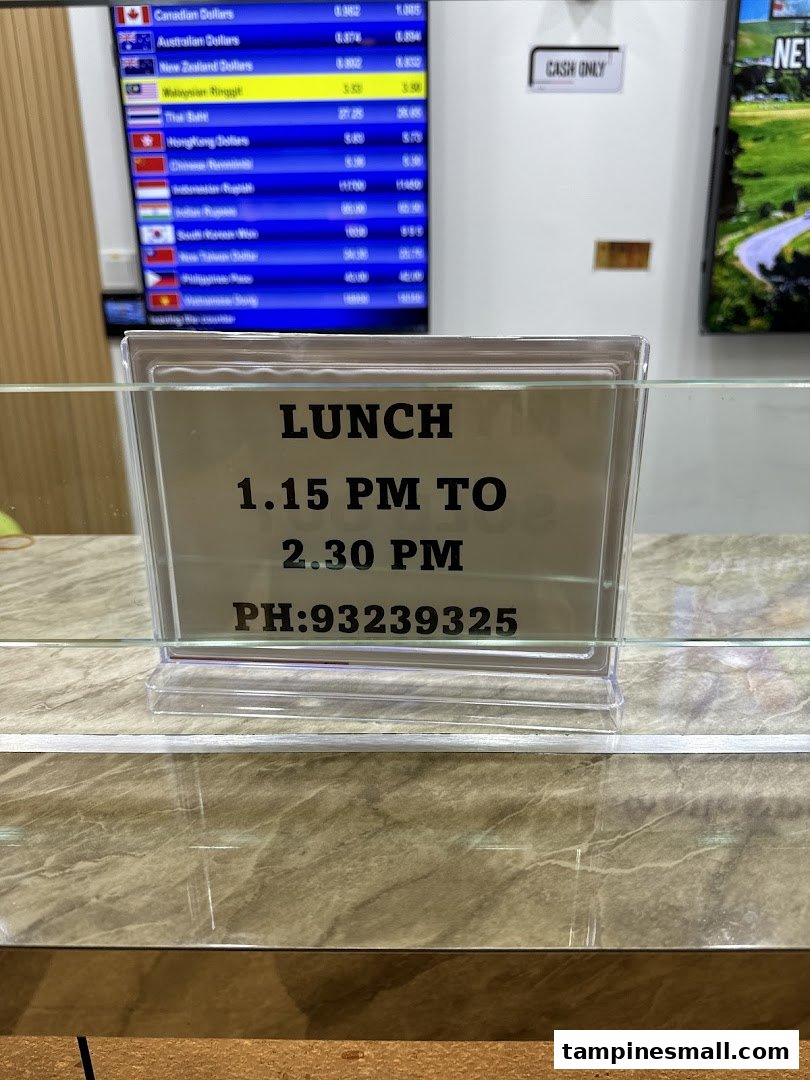 A sign displaying lunch hours and contact information, with a currency exchange rate board in the background.