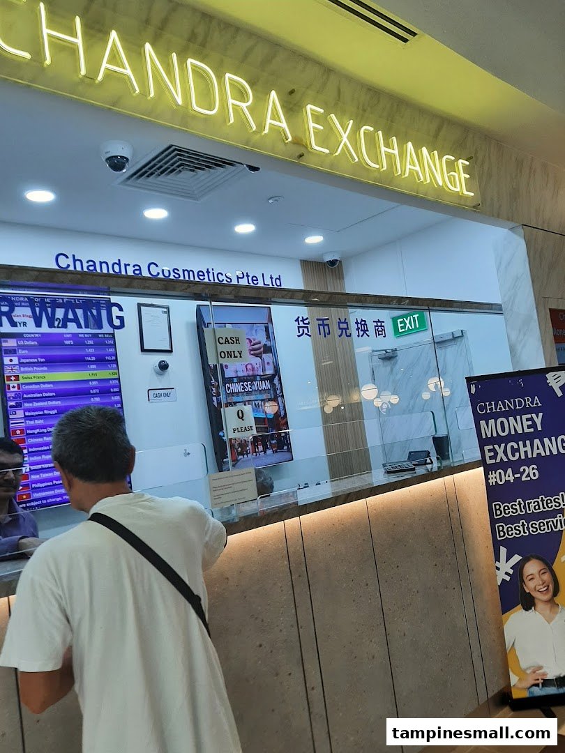 A customer at the counter of Chandra Money Exchange, showing the service area and currency rates.