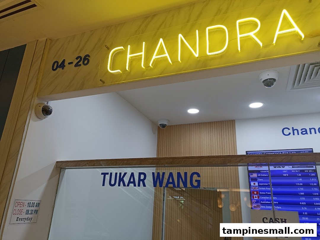 The illuminated entrance of Chandra Money Exchange, showing its name, unit number, and operating hours.