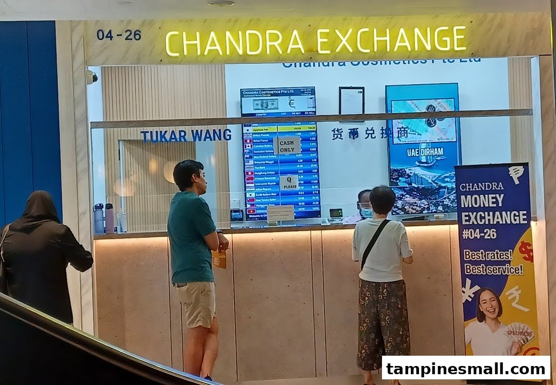 Customers at Chandra Money Exchange counter, with currency rates displayed on screens.