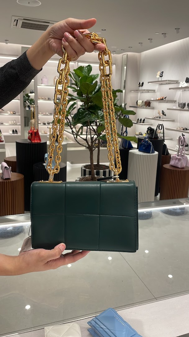 A person holds a stylish green handbag with a gold chain inside a CHARLES & KEITH store.
