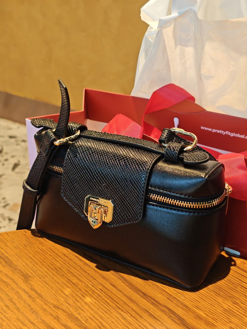 A stylish black handbag with gold hardware from CHARLES & KEITH, displayed on a wooden surface.